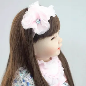 Natuurgetrouwe rebornpop met bruin haar, roze kanten hoofdband en bloemige outfit