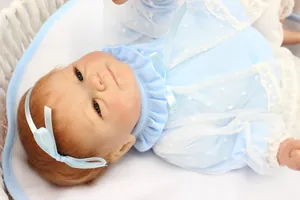 Gros plan d'une poupée reborn, cheveux bruns et vêtements en dentelle bleue, berceau