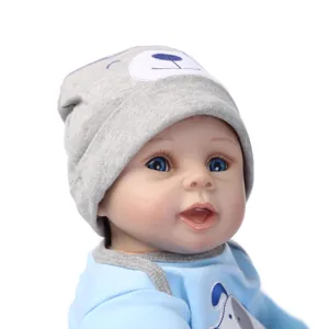 Realistic reborn baby doll in blue onesie and grey bear hat on white background