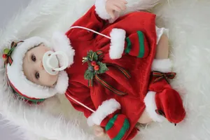 Dettaglio di una bambola reborn realistica con vestito natalizio rosso e decori di agrifoglio