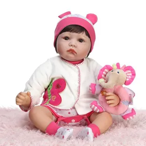 Realistic reborn baby doll in pink knit hat with elephant plush toy on soft pink rug