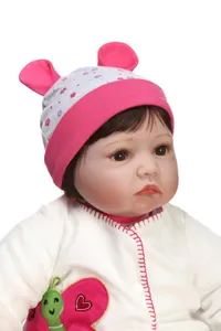 Close-up of a realistic reborn doll featuring pink baby hat and butterfly embroidery details