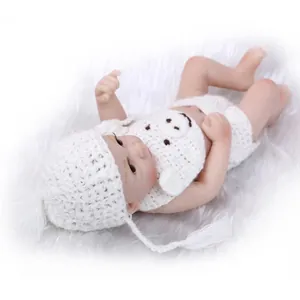 Realistic silicone baby doll wearing a white crochet outfit on a plush background