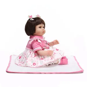Lifelike reborn baby doll with brown hair and pink floral outfit on white cushion