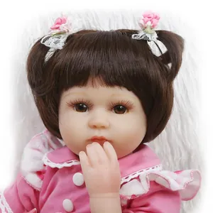 Realistic reborn baby doll with brown hair and pink floral dress on white plush background