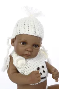 Close-up of a realistic black baby doll with a white knit hat and embroidered bear bib