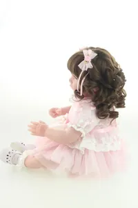 Detail of 20 inch reborn doll showing curly brown hair and pink sequin lace dress