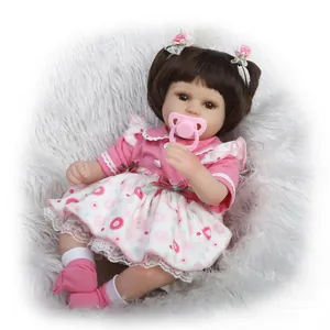 Realistic reborn baby doll with brown hair and pink heart dress on soft white plush