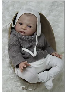 Lifelike reborn baby doll in grey knit top and white bonnet on plush display tray