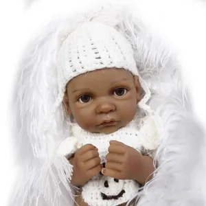 Miniature reborn baby doll with dark skin tone wearing white knit hat and smiley sweater