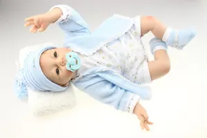 Detail of reborn baby doll in blue knit cardigan with pacifier on plush pillow