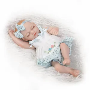 Miniature sleeping reborn doll in white embroidered dress on grey plush mat
