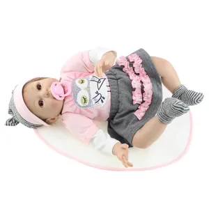 Poupée réaliste Reborn en tenue de hibou rose et jupe grise sur un tapis blanc