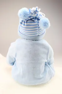 Close-up of lifelike reborn doll wearing a blue knitted hat with plush pom-poms from behind