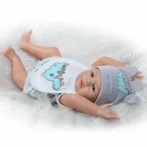 Realistische Reborn-Babypuppe im Dino-Outfit mit blauen Augen auf weißem Plüschgrund