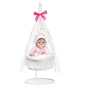 Realistic reborn baby doll in pink knit outfit sitting in a white hanging cradle chair