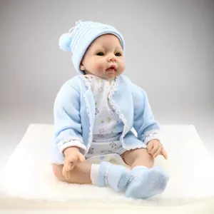 Realistic reborn baby doll in blue knit cardigan and hat on a white plush mat