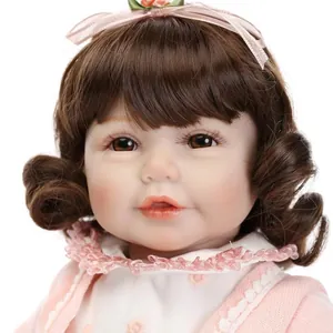 Lifelike reborn baby doll girl with brown curly hair and pink satin bow on white