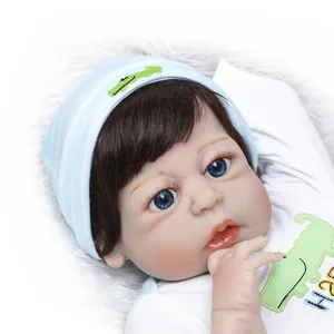 Realistische Reborn Babypuppe mit blauer Mütze und Dinosaurier-Top auf weißem Plüsch