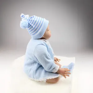 Handmade realistic reborn baby doll wearing a blue knit outfit on a soft plush white rug