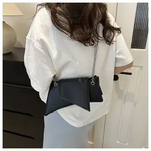 Detalle de un bolso bandolera geométrico negro con cadena plateada sobre camiseta blanca