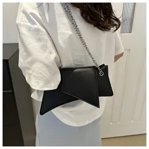 Detalle de un bolso bandolera geométrico negro con una elegante cadena de metal plateado