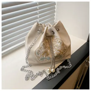 Detail of floral embroidery on ivory satin bucket bag with silver chain and pearl accents