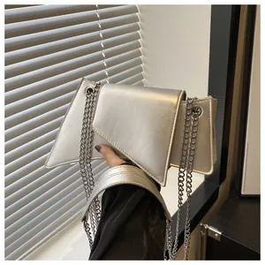 Detalle del bolso geométrico plateado con correa de cadena bajo luz y sombras naturales