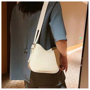Bolso hobo bicolor crema y caqui con correa ancha llevado por una modelo en un pasillo