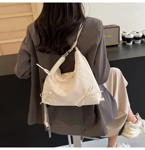 Détail d'un sac à bandoulière blanc cassé avec nœuds et chaîne dans un café chic