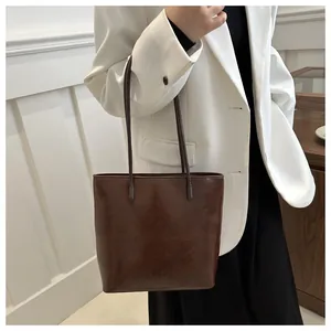 Close-up of a large coffee brown faux leather tote bag worn with a white blazer