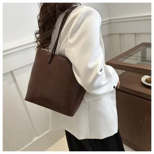 Dark brown leather tote bag showing minimalist design and slim shoulder straps on model