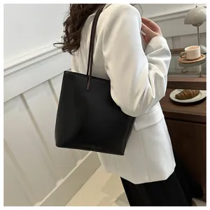 Detail of minimalist black leather tote bag with dark brown straps worn over the shoulder