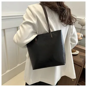 Detail of minimalist black leather tote bag with brown handles on a white blazer outfit