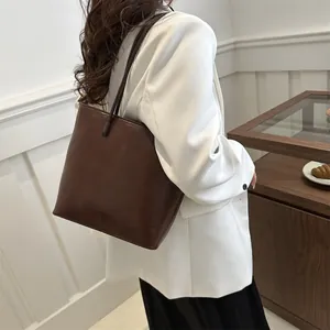 Minimalist large brown tote bag with glossy finish shown on model in a stylish setting