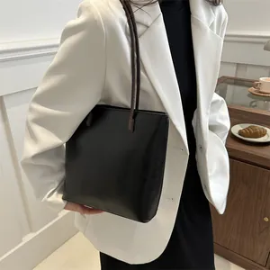 Minimalist black leather tote bag with brown shoulder straps worn by model in cozy interior
