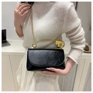 Détail du sac carré noir minimaliste avec sa poignée dorée en forme de trombone