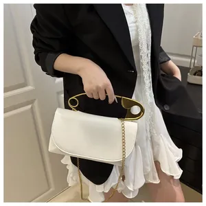 Détail d'un sac en cuir crème avec une poignée dorée en forme d'épingle de nourrice