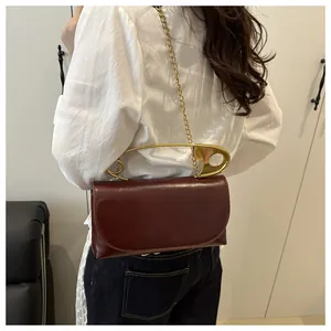 Détail du sac à bandoulière en cuir bordeaux avec poignée créative épingle dorée