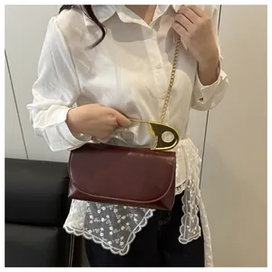 Gros plan sur un sac bordeaux avec une poignée trombone dorée unique et une bandoulière chaîne