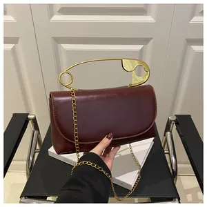 Détail du sac en cuir bordeaux avec une poignée épingle de sûreté dorée et chaînette
