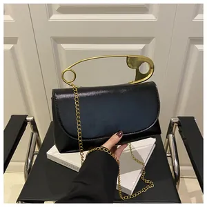 Détail d'un sac à main noir avec poignée épingle de sûreté dorée et bandoulière chaîne