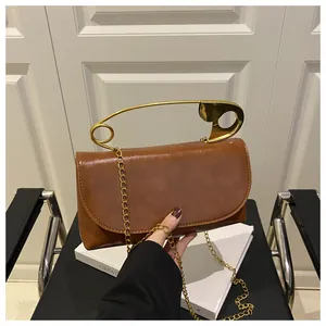 Détail d'un sac bandoulière marron avec poignée dorée en forme d'épingle de nourrice