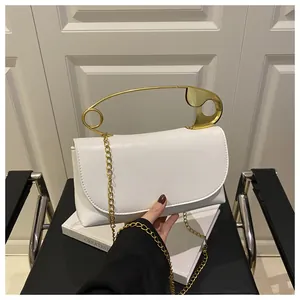 Détail d'un sac en cuir blanc avec une poignée dorée unique en forme de grand trombone