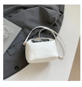 Dettaglio di una borsa a tracolla bianca lucida con finiture dorate su una giacca grigia