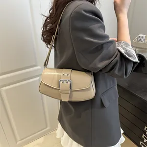 Chic beige glossy leather underarm bag with silver buckle worn by a woman in a suit