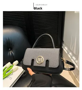 Detail einer eleganten schwarzen und grauen Handtasche mit goldenem M-Logo und Griff