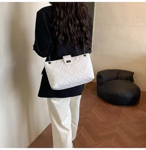 Detail view of white quilted tote bag with metal chain strap and turn-lock closure on model