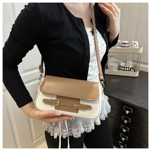 Chic beige and white crossbody bag with gold buckles shown on a model in a cozy setting