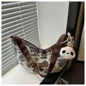 Detail of printed canvas crescent bag with panda charm and brown adjustable strap